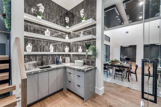 bar featuring gray cabinets, sink, a towering ceiling, and light wood-type flooring