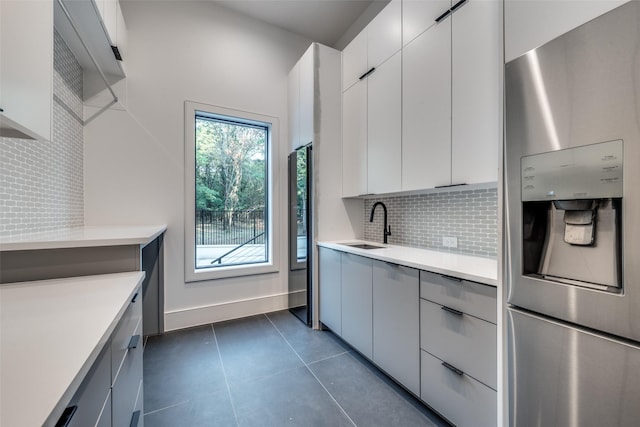 kitchen with stainless steel fridge, tasteful backsplash, dark tile patterned floors, sink, and white cabinets