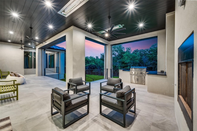 patio terrace at dusk featuring grilling area, an outdoor hangout area, ceiling fan, and exterior kitchen