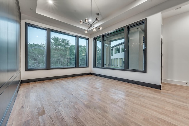 unfurnished room with light hardwood / wood-style floors, a raised ceiling, and a notable chandelier