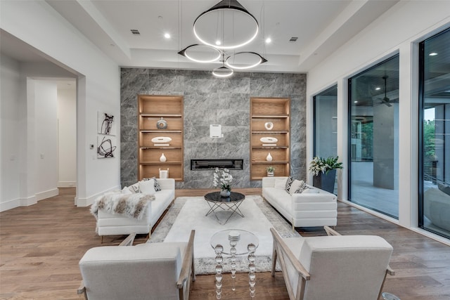 living room with a raised ceiling, built in shelves, a high end fireplace, and wood-type flooring