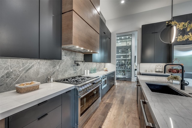 kitchen with light stone countertops, stainless steel appliances, wall chimney range hood, sink, and decorative light fixtures