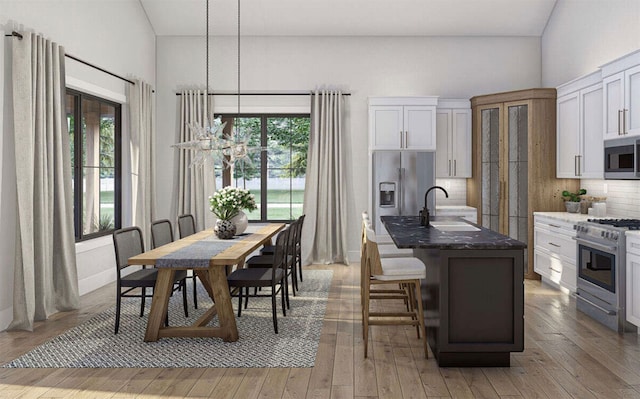 kitchen with an island with sink, appliances with stainless steel finishes, white cabinetry, light hardwood / wood-style flooring, and decorative light fixtures