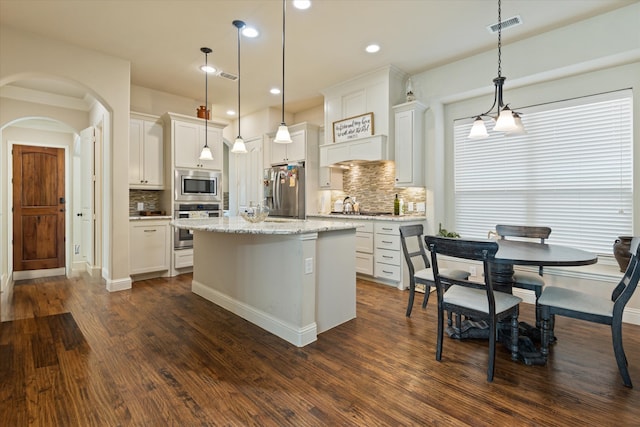 kitchen with hanging light fixtures, a kitchen island, white cabinetry, dark wood-type flooring, and stainless steel appliances