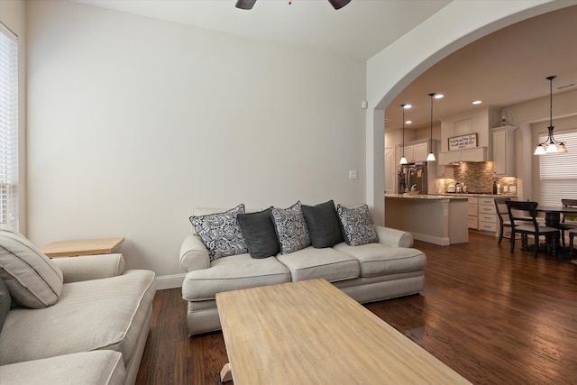 living room featuring dark wood-type flooring, plenty of natural light, and ceiling fan with notable chandelier