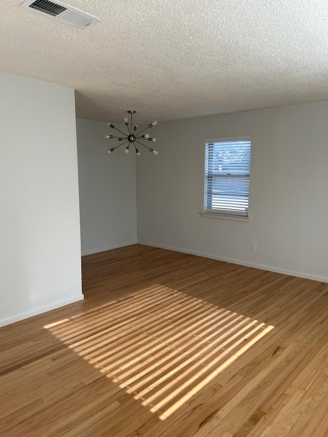 empty room featuring a chandelier, light hardwood / wood-style flooring, and a textured ceiling