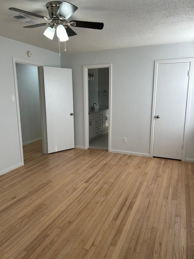 unfurnished bedroom featuring ceiling fan, a textured ceiling, ensuite bathroom, and light wood-type flooring