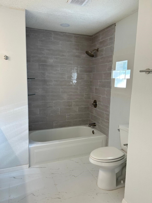 bathroom featuring tiled shower / bath, a textured ceiling, and toilet