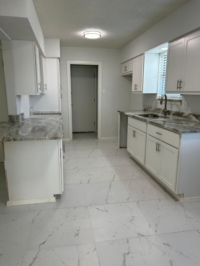 kitchen with a textured ceiling, sink, and white cabinets