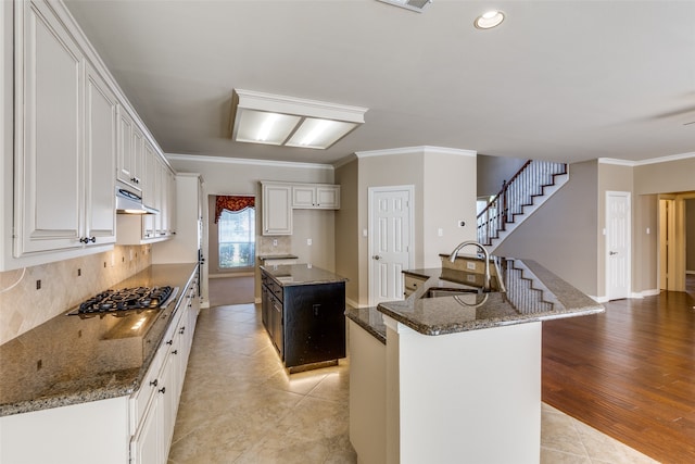 kitchen with stainless steel gas cooktop, light hardwood / wood-style floors, white cabinets, ornamental molding, and a center island with sink