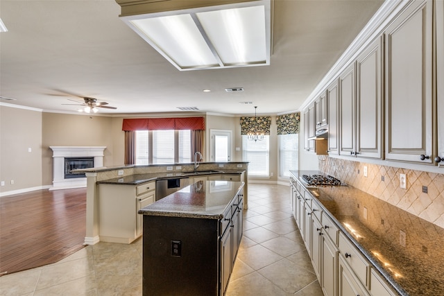 kitchen with light hardwood / wood-style flooring, crown molding, dark stone counters, and a kitchen island with sink