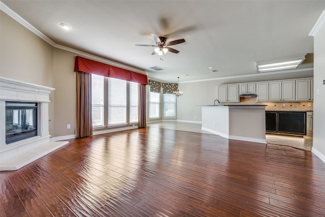 unfurnished living room with dark wood-type flooring, crown molding, and ceiling fan with notable chandelier