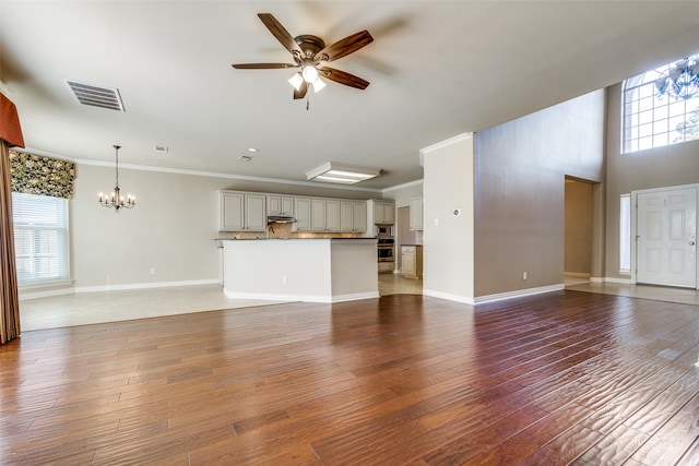 unfurnished living room featuring hardwood / wood-style flooring, ornamental molding, and ceiling fan with notable chandelier