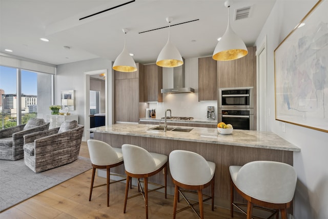 kitchen featuring wall chimney exhaust hood, a kitchen bar, light stone counters, and pendant lighting