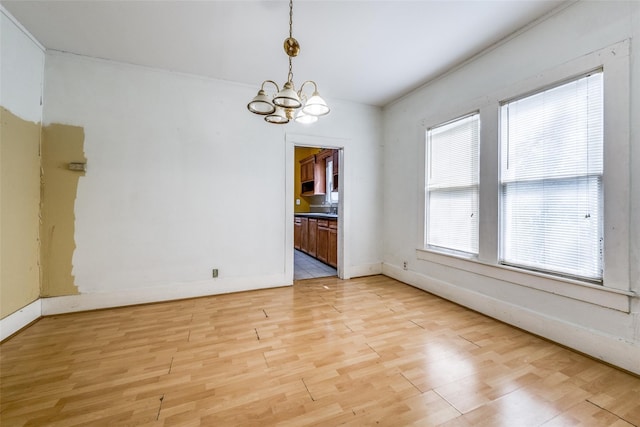 empty room with a wealth of natural light, light hardwood / wood-style flooring, and an inviting chandelier