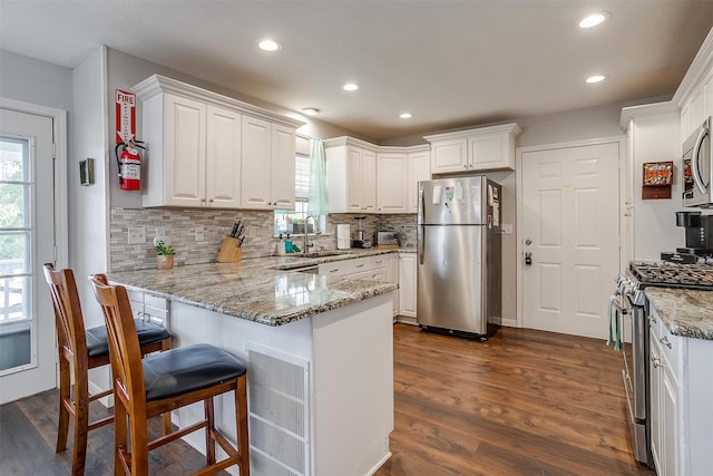 kitchen with backsplash, dark hardwood / wood-style flooring, kitchen peninsula, white cabinetry, and stainless steel appliances