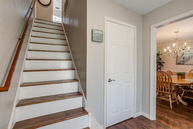 stairs with crown molding, wood-type flooring, and an inviting chandelier