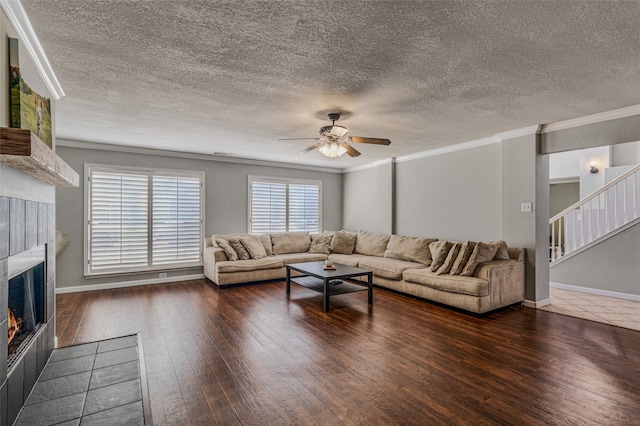 living room featuring ornamental molding, a textured ceiling, dark hardwood / wood-style flooring, a tile fireplace, and ceiling fan