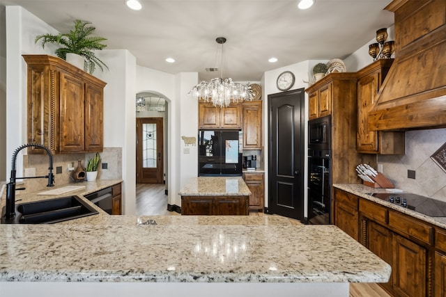 kitchen featuring light stone countertops, sink, light hardwood / wood-style flooring, a kitchen island, and black appliances