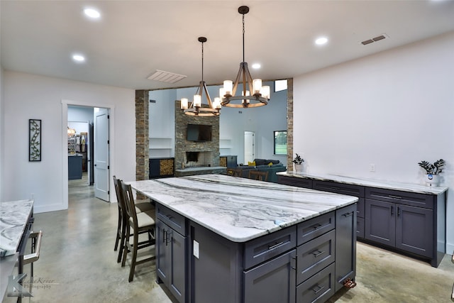 kitchen featuring hanging light fixtures, a breakfast bar, a fireplace, a notable chandelier, and a center island