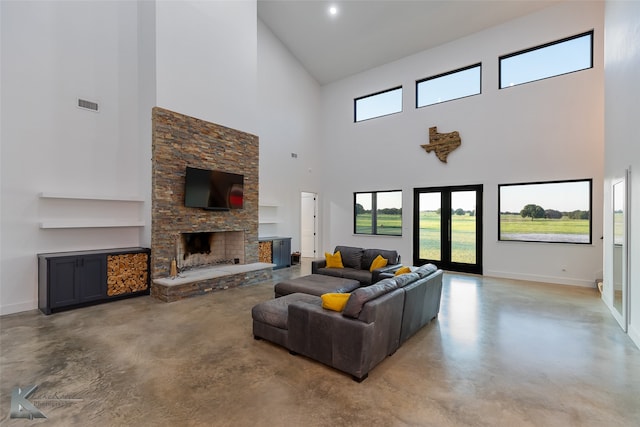 living room featuring a towering ceiling, concrete floors, french doors, and a stone fireplace