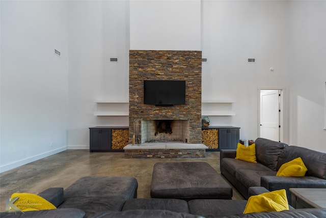 living room featuring a stone fireplace, concrete floors, and a high ceiling