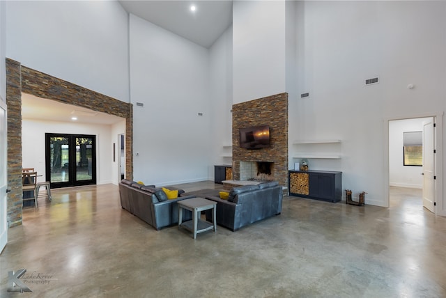 living room featuring a high ceiling, concrete flooring, french doors, and a stone fireplace