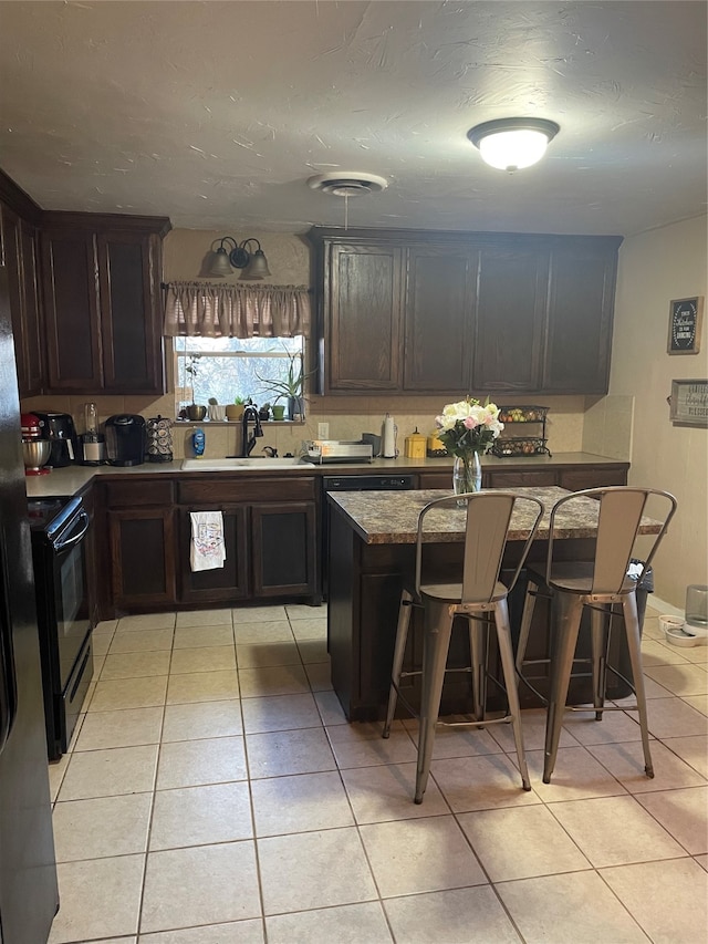 kitchen with black electric range oven, light tile patterned floors, a kitchen breakfast bar, sink, and a center island