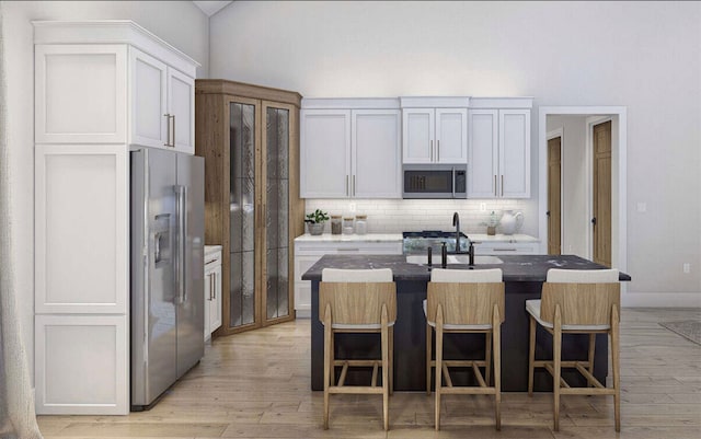 kitchen with appliances with stainless steel finishes, light wood-type flooring, white cabinets, a breakfast bar area, and a center island with sink