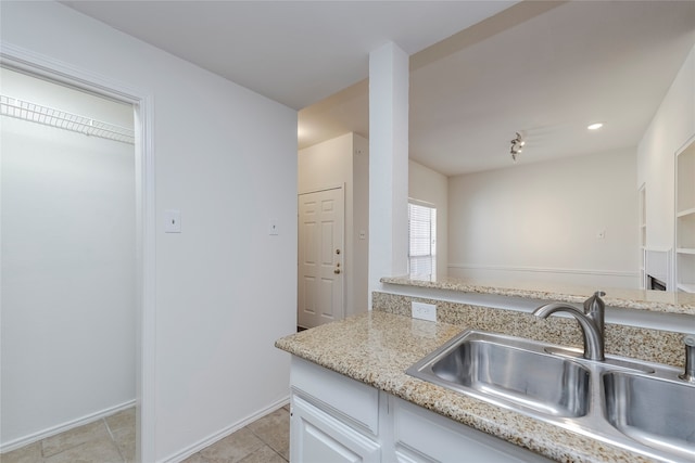 kitchen featuring light stone countertops, sink, white cabinets, and light tile patterned flooring