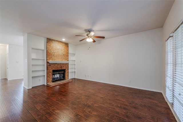 unfurnished living room with a brick fireplace, ceiling fan, built in shelves, and dark hardwood / wood-style flooring