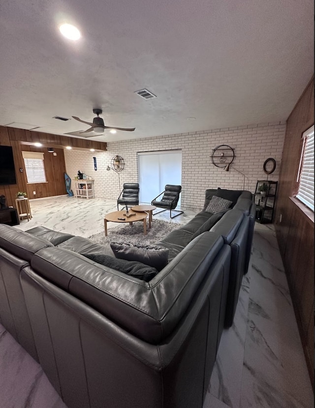 interior space with a textured ceiling, wooden walls, brick wall, and ceiling fan