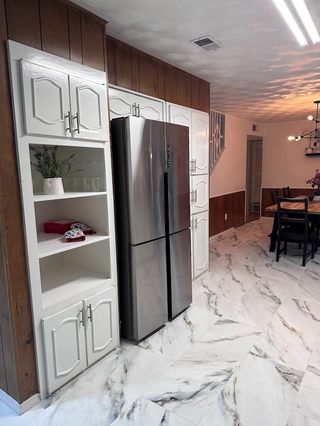 kitchen with an inviting chandelier, stainless steel fridge, dark brown cabinetry, and wooden walls