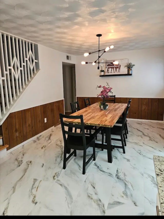 dining room with an inviting chandelier and wood walls