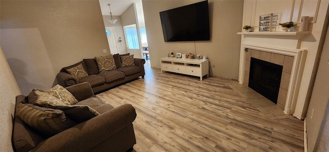 living room with a tiled fireplace, light wood-type flooring, and vaulted ceiling