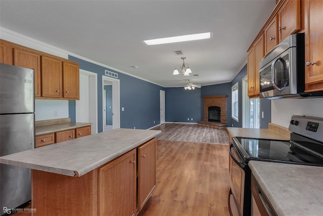 kitchen featuring a kitchen island, stainless steel appliances, a fireplace, light hardwood / wood-style floors, and decorative light fixtures