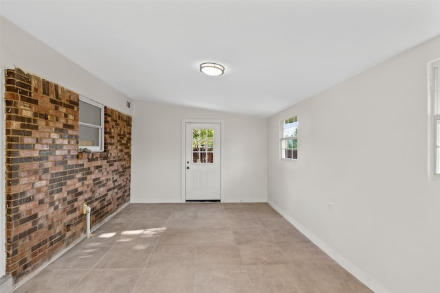 tiled empty room featuring lofted ceiling and brick wall