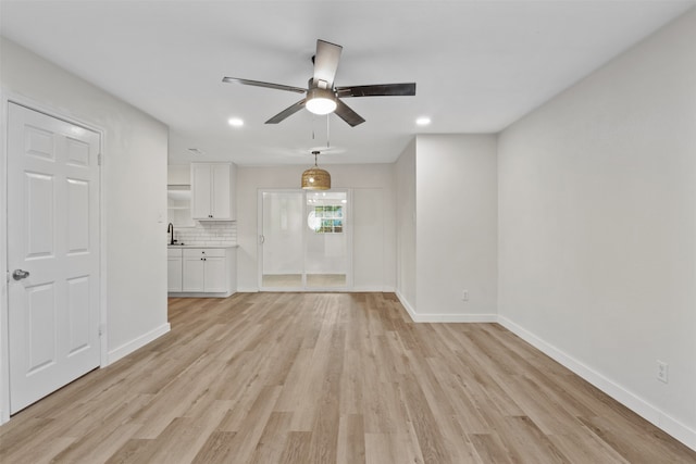 unfurnished living room featuring ceiling fan, sink, and light wood-type flooring