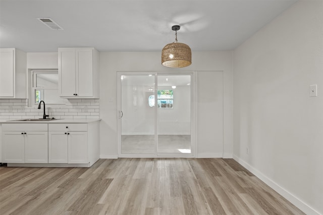 kitchen featuring backsplash, white cabinets, hanging light fixtures, and light wood-type flooring