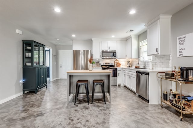 kitchen with sink, a kitchen island, a kitchen breakfast bar, stainless steel appliances, and white cabinets