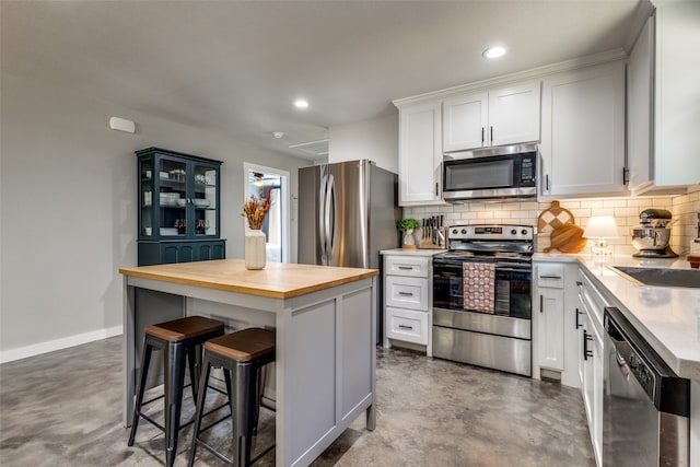 kitchen with a kitchen island, white cabinets, a kitchen bar, concrete flooring, and appliances with stainless steel finishes