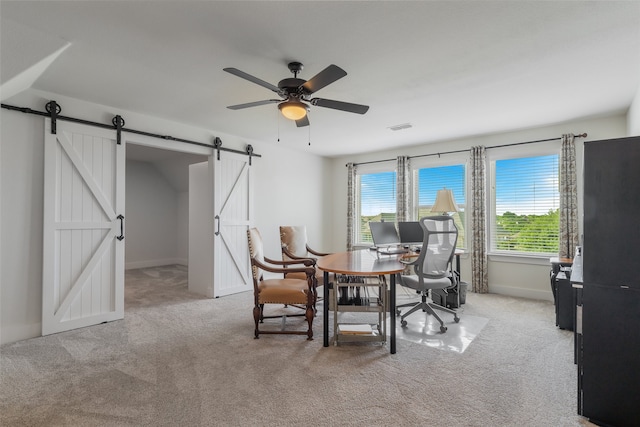 dining room with ceiling fan, a barn door, and light colored carpet