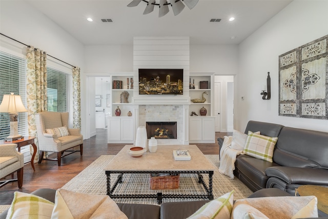 living room featuring wood-type flooring, a large fireplace, and ceiling fan