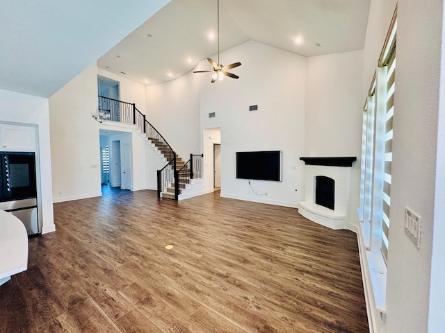 unfurnished living room featuring ceiling fan, high vaulted ceiling, wood-type flooring, and a brick fireplace