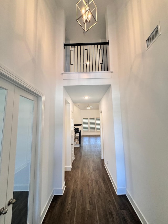 hallway with dark wood-type flooring, an inviting chandelier, and a towering ceiling