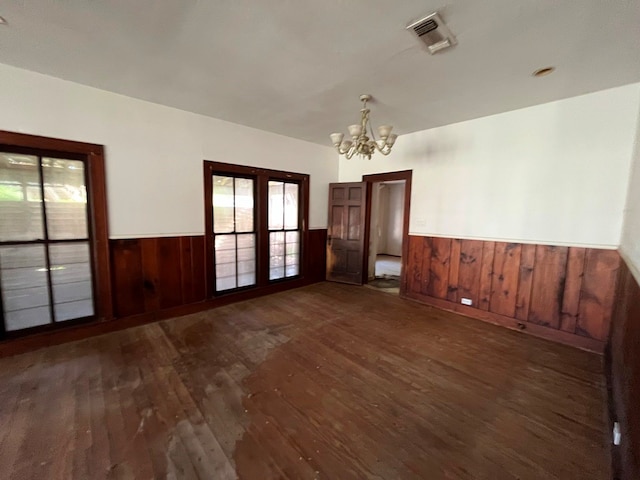 spare room featuring a notable chandelier, french doors, wooden walls, and dark wood-type flooring