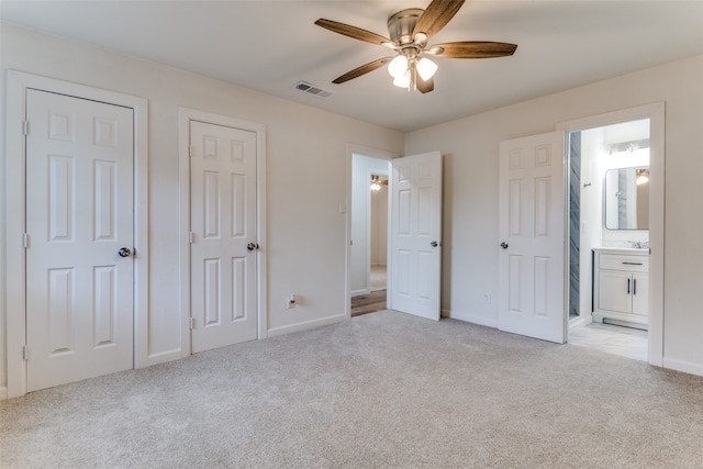 unfurnished bedroom featuring light carpet, multiple closets, ensuite bath, and ceiling fan