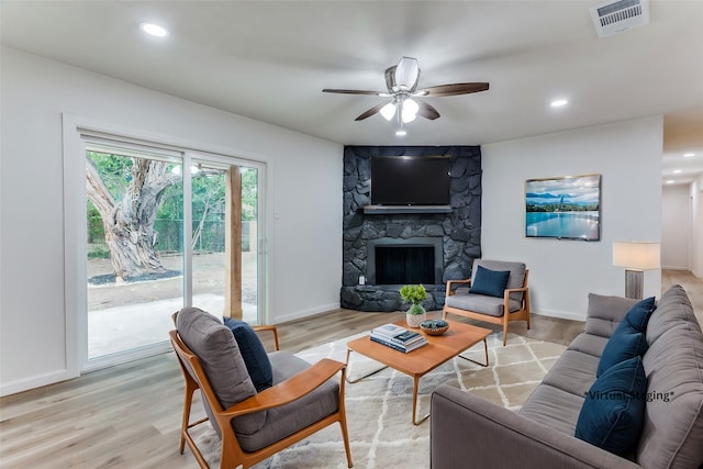 living room featuring ceiling fan, light wood-type flooring, and a fireplace