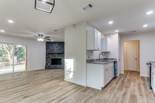 kitchen featuring a stone fireplace, white cabinets, light wood-type flooring, dark stone countertops, and sink