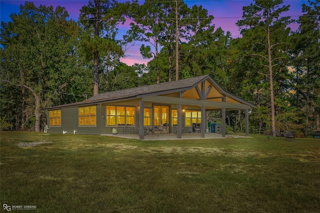 back house at dusk featuring a patio area and a lawn